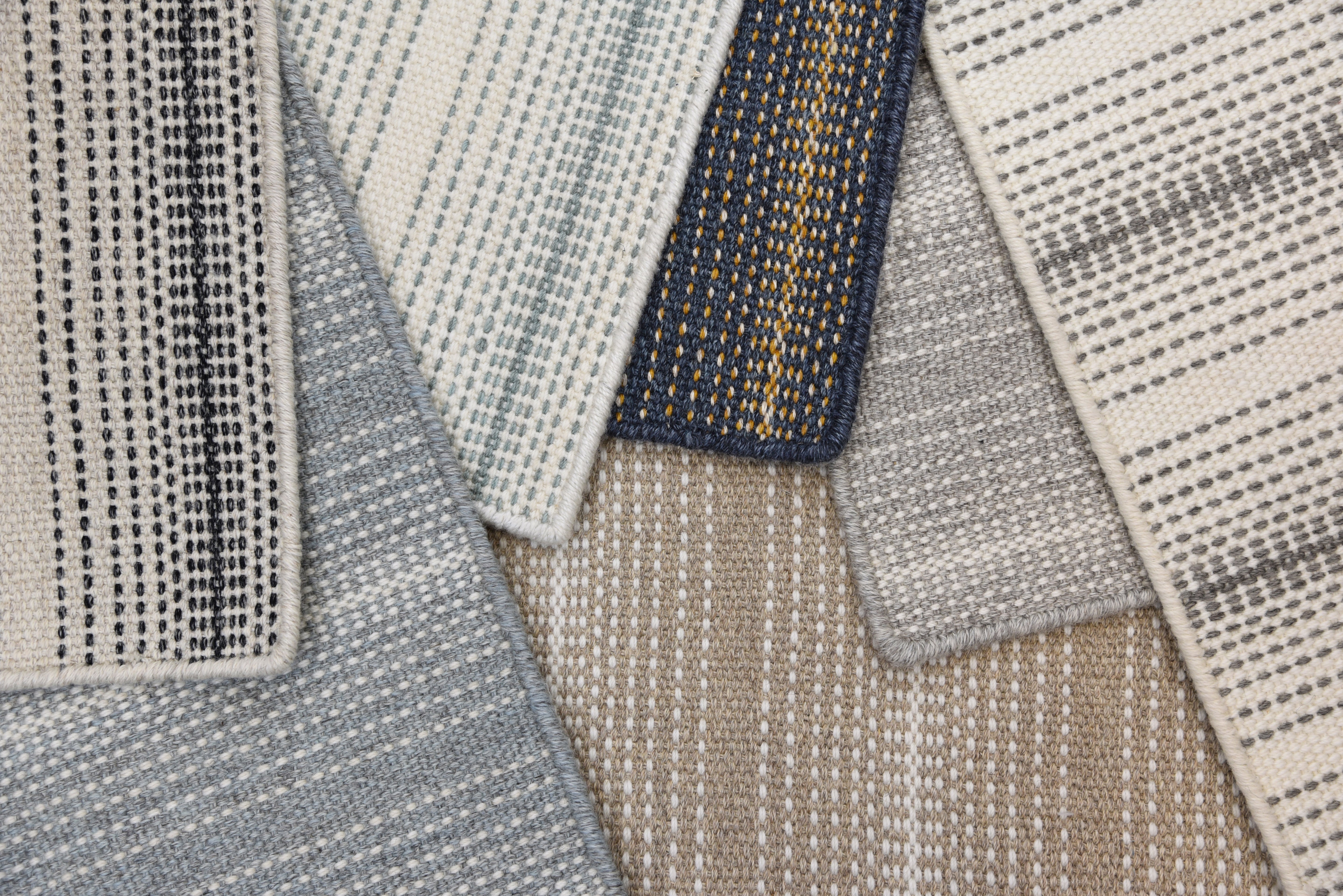 Close-up of multiple textured striped rugs in assorted neutral colors overlapping each other