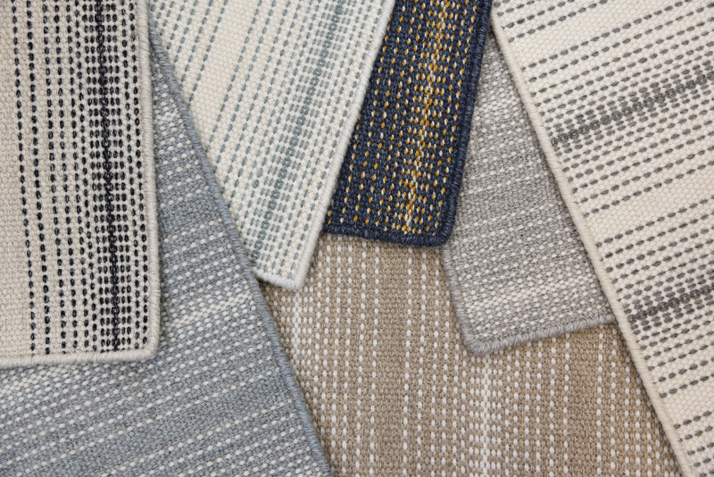 Close-up of multiple textured striped rugs in assorted neutral colors overlapping each other